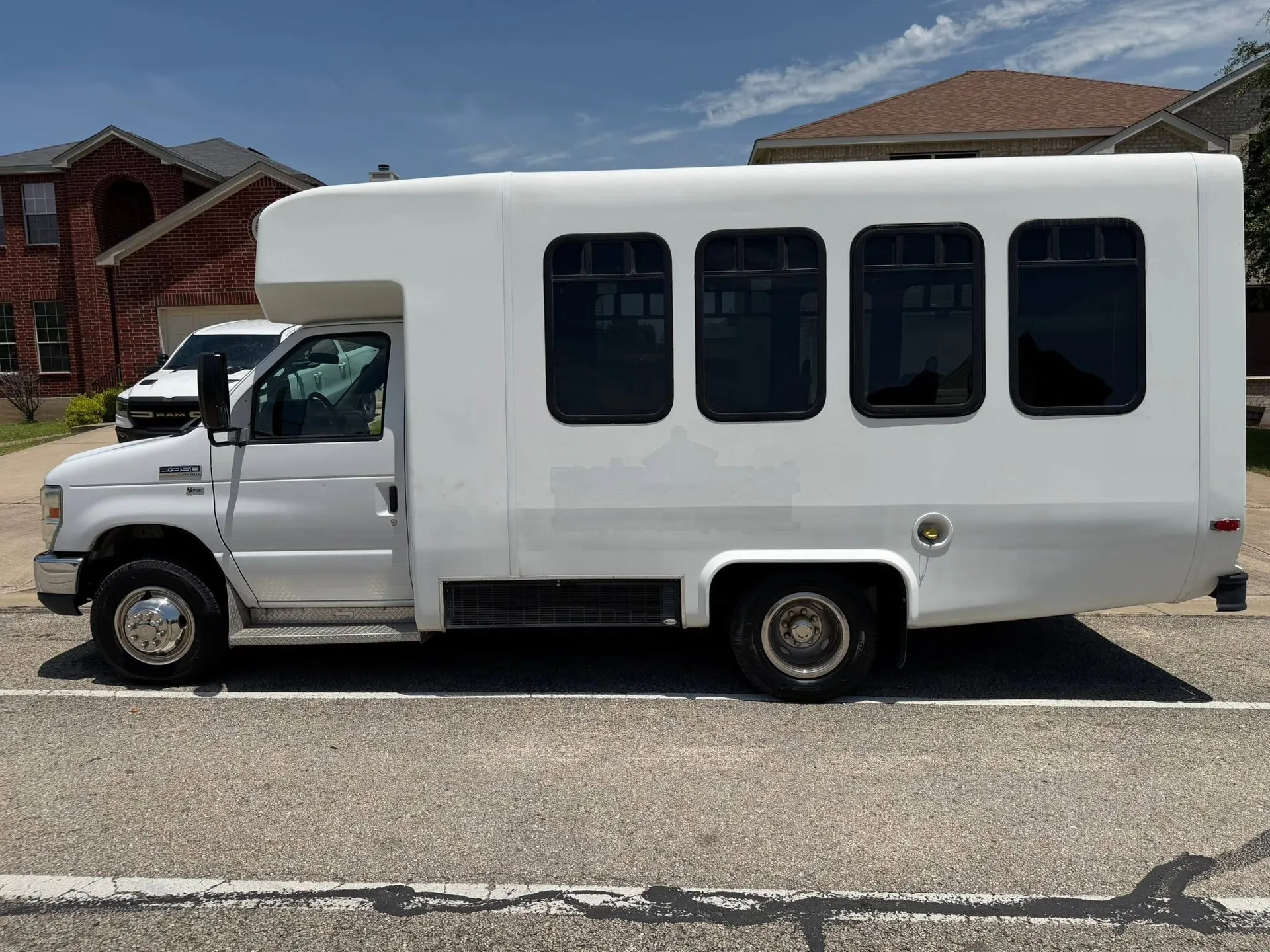 Real 2013 Ford E-350 minibus in side profile on a sunny residential street in front of a brick house